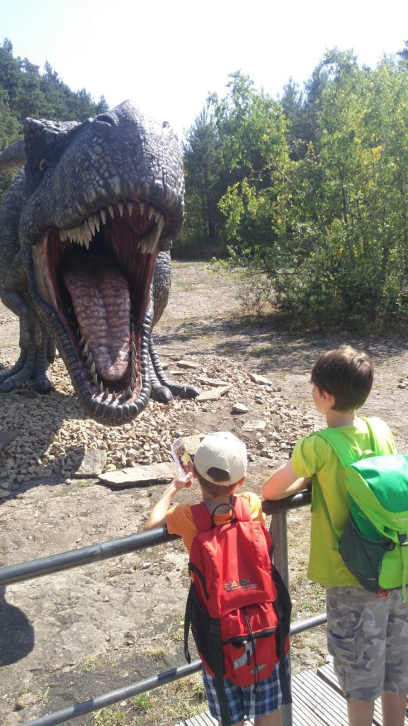 Zwei Jungen vor einer lebensgroßen Tyrannosaurus Rex Figur, die das Maul aufreißt.