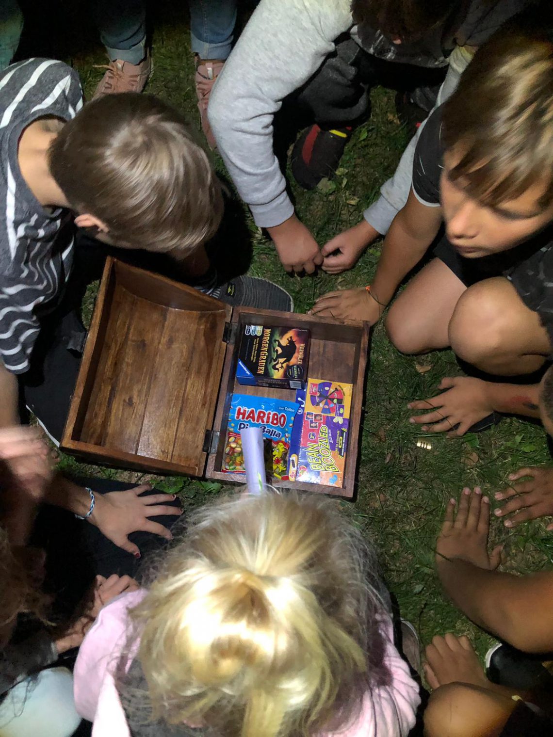 Mehrere Kinder um eine Schatzkiste aus Holz mit Süßigkeiten darin.