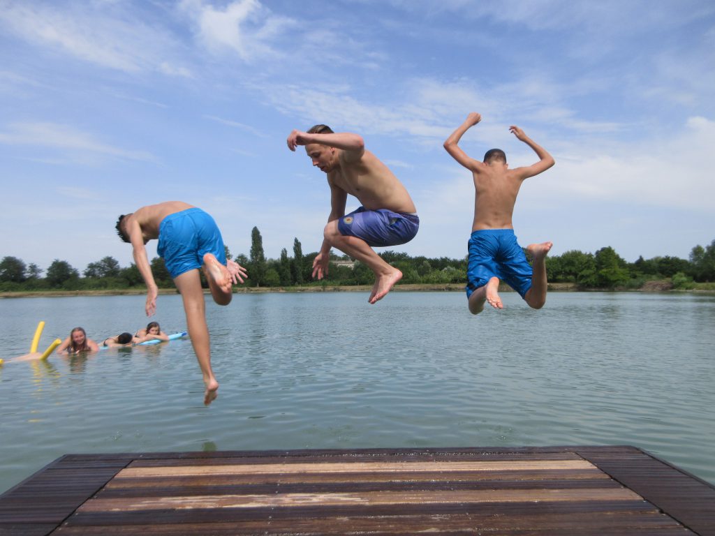 Drei Jungen, die gleichzeitig von einem Steg ins Wasser springen.